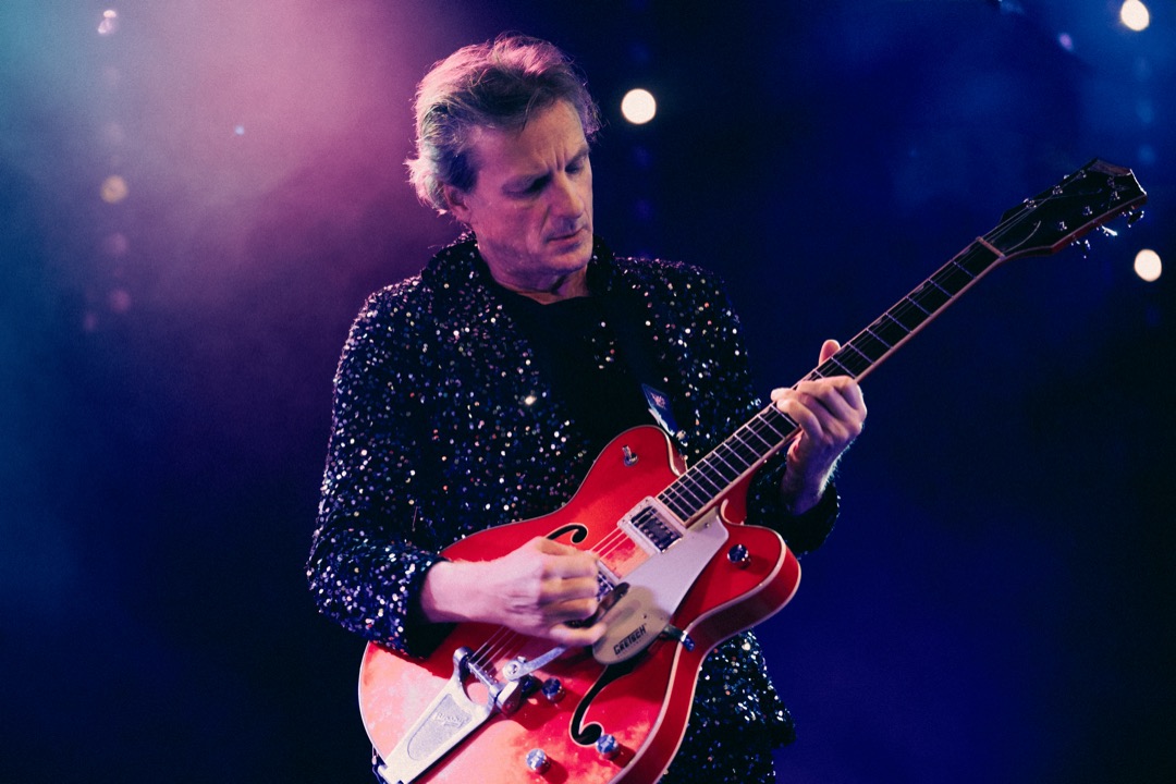 Fritz Schmutz spielt konzentriert E-Gitarre im bunten Bühnenlicht.